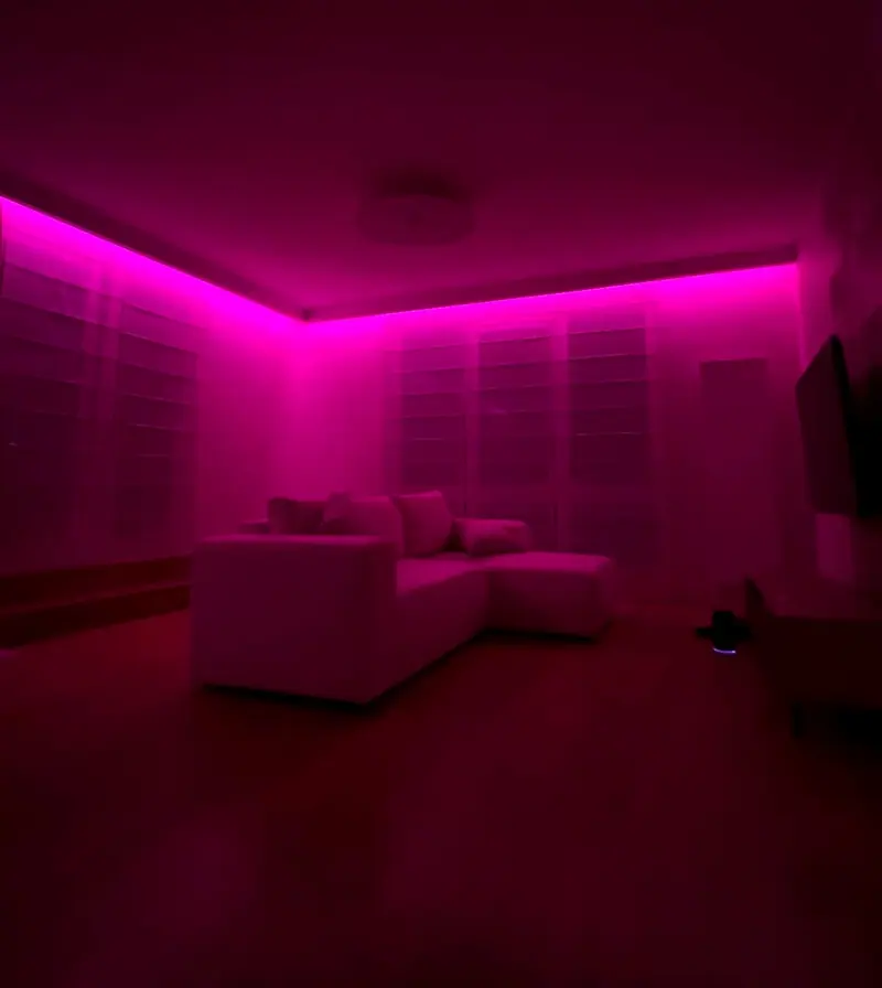 Salon z narożną sofą oświetlony różowym światłem taśmy LED RGB ukrytej we wnęce sufitu